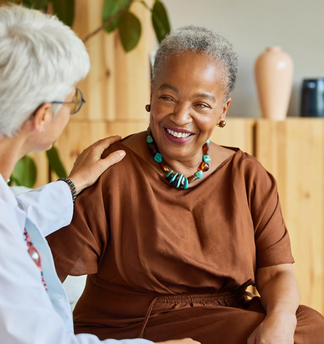 Two people talking.  The woman facing the camera is older and wearing a bright necklace.